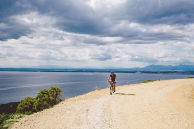Genç adam İspanya 'da bisiklet yolunda dağ bisikleti sürüyor. Bir dağ bisikleti süren sporcu Akdeniz 'in arka planında Costa Brava' ya karşı off-road yapıyor. İspanya 'da bisiklet