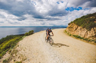Genç adam İspanya 'da bisiklet yolunda dağ bisikleti sürüyor. Bir dağ bisikleti süren sporcu Akdeniz 'in arka planında Costa Brava' ya karşı off-road yapıyor. İspanya 'da bisiklet
