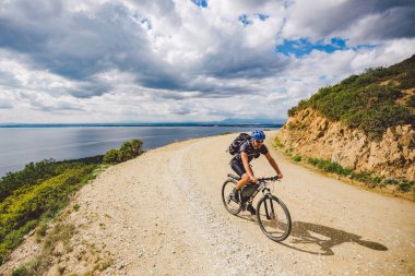 Genç adam İspanya 'da bisiklet yolunda dağ bisikleti sürüyor. Bir dağ bisikleti süren sporcu Akdeniz 'in arka planında Costa Brava' ya karşı off-road yapıyor. İspanya 'da bisiklet