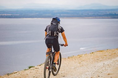 Genç adam İspanya 'da bisiklet yolunda dağ bisikleti sürüyor. Bir dağ bisikleti süren sporcu Akdeniz 'in arka planında Costa Brava' ya karşı off-road yapıyor. İspanya 'da bisiklet