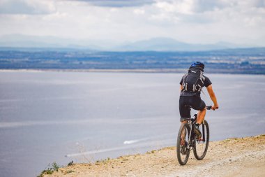 Genç adam İspanya 'da bisiklet yolunda dağ bisikleti sürüyor. Bir dağ bisikleti süren sporcu Akdeniz 'in arka planında Costa Brava' ya karşı off-road yapıyor. İspanya 'da bisiklet