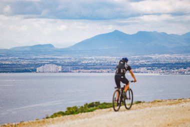 Genç adam İspanya 'da bisiklet yolunda dağ bisikleti sürüyor. Bir dağ bisikleti süren sporcu Akdeniz 'in arka planında Costa Brava' ya karşı off-road yapıyor. İspanya 'da bisiklet