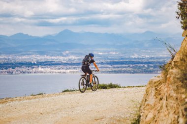 Genç adam İspanya 'da bisiklet yolunda dağ bisikleti sürüyor. Bir dağ bisikleti süren sporcu Akdeniz 'in arka planında Costa Brava' ya karşı off-road yapıyor. İspanya 'da bisiklet