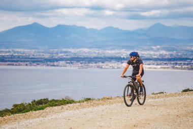 Genç adam İspanya 'da bisiklet yolunda dağ bisikleti sürüyor. Bir dağ bisikleti süren sporcu Akdeniz 'in arka planında Costa Brava' ya karşı off-road yapıyor. İspanya 'da bisiklet