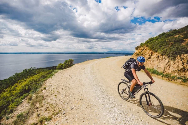 Genç adam İspanya 'da bisiklet yolunda dağ bisikleti sürüyor. Bir dağ bisikleti süren sporcu Akdeniz 'in arka planında Costa Brava' ya karşı off-road yapıyor. İspanya 'da bisiklet