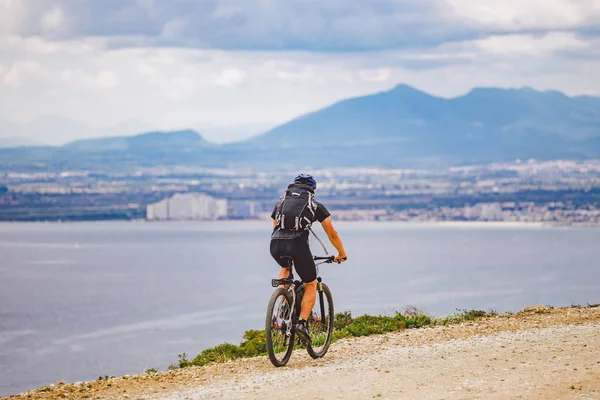 Молодой парень катается на горном велосипеде по велосипедному маршруту в Испании. Спортсмен на горном велосипеде едет по бездорожью на фоне Средиземного моря, Коста Брава. Велоспорт в Испании — стоковое фото