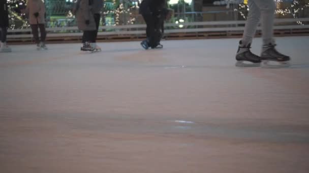 Felismerhetetlen emberek lábai lovagolnak egy város jégpályáján esténként. Téli korcsolyapálya a karácsonyi vásáron. Az emberek korcsolyázni a pályán Kijevben, Ukrajnában a szerződés területén — Stock videók