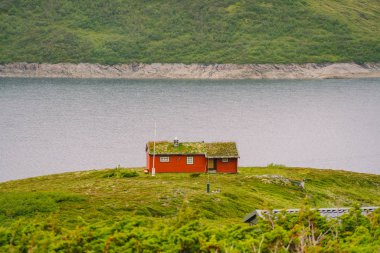 Norveç ahşap yazlığı manzaralı göl manzaralı, Norveç, İskandinavya. Kırsal kesimdeki göl kıyısındaki kır evi. Göl kıyısındaki turba çatılı kulübe. Norveç 'te tipik bir çim çatı kulübesi. Tipik kırmızı rorbu balıkçı kulübesi.