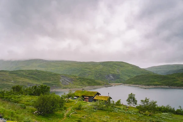 Norweski drewniany domek letni z widokiem na malownicze jezioro, Norwegia, Skandynawia. Domek nad jeziorem na wsi. Chata pokryta torfem nad jeziorem. Typowa chata pokryta trawą w Norwegii. Typowa czerwona chatka rybacka rorbu — Zdjęcie stockowe