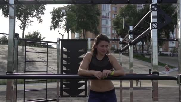 Attraktive, fitte junge Frau in Sportkleidung ruhen sich auf dem Streetworkout-Bereich aus. den gesunden Lebensstil in der Stadt. Straßenporträt starke Frau posiert im Fitnessstudio. schöne athletische Frau in Sport-BH posiert — Stockvideo