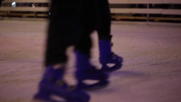 Nogi nierozpoznawalnych ludzi jeżdżą wieczorami po otwartym lodowisku. Zimowe wrotki na jarmarku bożonarodzeniowym. Ludzie jeżdżą na wrotkach w Kijowie, Ukraina na obszarze objętym umową — Wideo stockowe