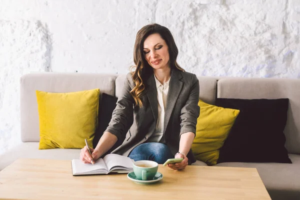 Escrever laticínios no caderno no café, conceito como memória da vida. mulher com telefone celular e caneta na mesa de madeira com xícara de café no café. Sorrindo Empresária Fazendo Notas Bloco de Notas — Fotografia de Stock