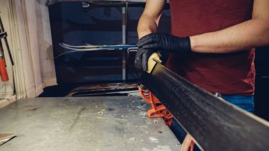 Kayak servisi atölyesinde çalışan erkek kayakları bileyip onarıyor. Kayak kenarlarını, elmas taşla tutturulmuş kenar ayarlama aleti ile keskinleştiriyorum. Kayak kaldırımının tema onarımı