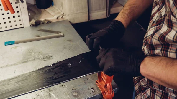 Mantenimiento de esquí. Eliminando el exceso de cera del raspador de plástico de la base de esquí de carrera. Servicio de esquí y reparación. Trabajador de invierno haciendo reparación de bases. Servicio de alquiler de taller. Reparador en servicio de esquí de taller —  Fotos de Stock