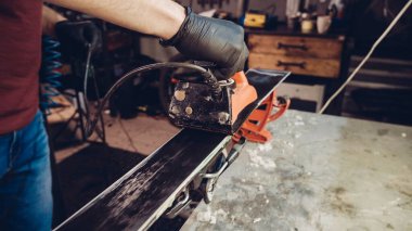 Kayak tabanına demirle sıcak mum sürüyorum. Kayak tabanına kayak cilası sürüyorum. Kayak zemini ayarlaması. Kayak demiri ve balmumu çubukları. Kayak servisi ve onarım. Atölye kayak servisinde tamirci. Atölyede Kayak Yapan Adam