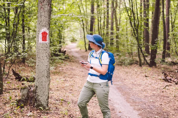 Hiking marked trail in the forest. Marking the tourist route painted on the tree. Touristic route sign. Travel route sign. Tourist hiker with backpack navigation uses smart phone