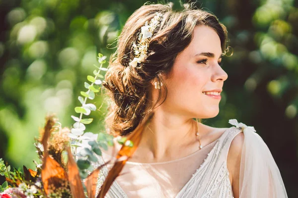 Schöne Braut mit Blumenstrauß steht auf Waldhintergrund. rustikaler Stil. schöne Braut in zartem Kleid im Freien. Nahaufnahme Porträt der jungen Braut im Park bei sonnigem Wetter Waldgebiet — Stockfoto