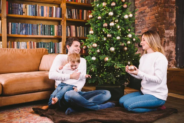 Сімейна різдвяна концепція. Прекрасна родина сидить біля ялинки в зимовий вечір. Щаслива сім'я з сином на підлозі біля дивана Вдома. Сім'я вдома в новорічний час. сім'я насолоджується новорічними святами — стокове фото