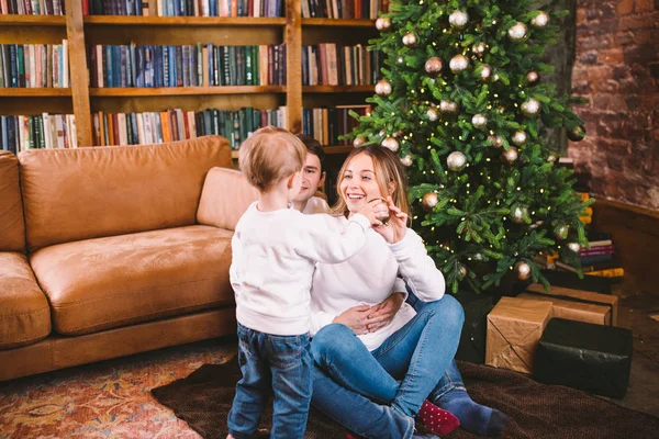 Conceito de Natal de Família. Linda família senta-se perto da árvore de Natal na noite de inverno. Família feliz com filho no chão perto do sofá em casa. Família em casa no Ano Novo. família desfrutar de feriados de ano novo — Fotografia de Stock