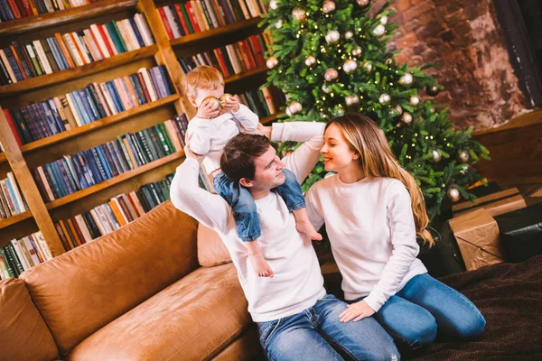 Concepto de Navidad familiar. La encantadora familia se sienta cerca del árbol de Navidad en la noche de invierno. Familia feliz con hijo en el suelo cerca del sofá En casa. Familia en casa en Año Nuevo. familia disfrutar de vacaciones de año nuevo — Foto de Stock