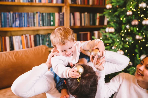 Concepto de Navidad familiar. La encantadora familia se sienta cerca del árbol de Navidad en la noche de invierno. Familia feliz con hijo en el suelo cerca del sofá En casa. Familia en casa en Año Nuevo. familia disfrutar de vacaciones de año nuevo — Foto de Stock