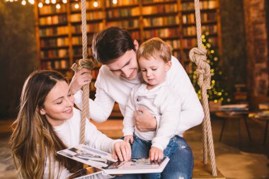 Noel arifesinde, Bebekli Aile 'nin evde dinlenmesi rahat, karanlık oturma odasında salıncak koltuğu. Ailesi tahterevallide eğleniyor. Aile ve çocukla kış akşamı. Oturma odasında Aile Okuma Kitabı