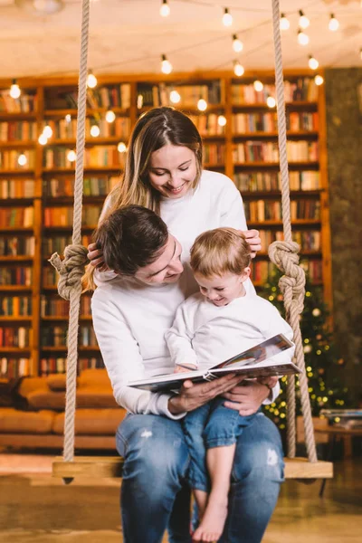 La unión familiar. Mamá, papá e hijo leyendo el libro de cuentos juntos sentados en casa. Family and Parenthood Concept. Familia feliz lee libro de niños mientras está sentado en casa en el interior del loft — Foto de Stock