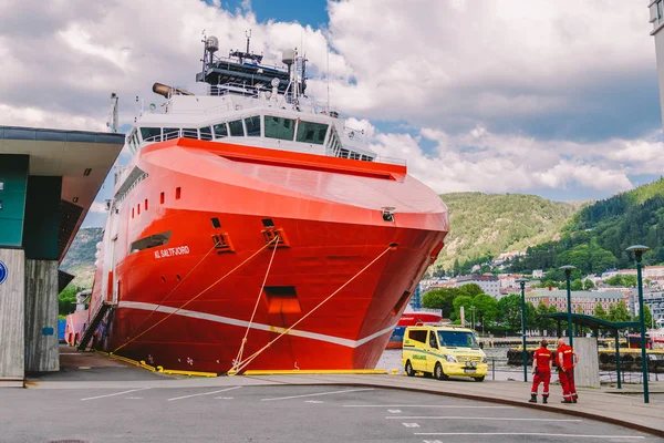 Dois paramédicos noruegueses em uniformes vermelhos estão descansando perto de uma ambulância estacionada em um porto perto de um grande navio. Medicina e cuidados de saúde temáticos em Noruega, Bergen julho 28, 2019 — Fotografia de Stock