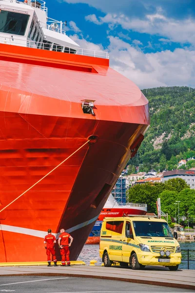 Dos paramédicos noruegos con uniformes rojos están descansando cerca de una ambulancia estacionada en un puerto cerca de un gran barco. Tema Salud y medicina en Noruega, Bergen julio 28, 2019 —  Fotos de Stock