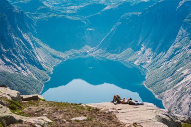 26 Temmuz 2019. Norveç. Hayalperest bir adam kayanın üzerinde uzanmış, arka planda mavi su fiyorduyla yamaçta yürüyüş yaptıktan sonra dinleniyor. Norveç gezisi, özgürlük konsepti. En tepedeki turist telefon kullanıyor