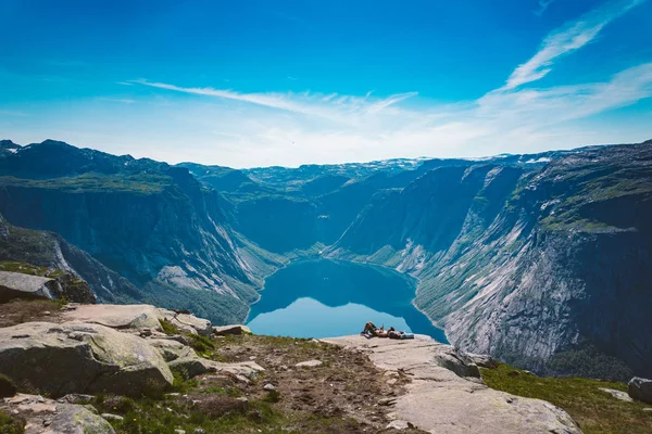2019年7月26日。 挪威。 人类梦想家躺在石头上，带着蓝色的水弦在悬崖顶上登山后放松了下来。 挪威之行，自由概念。 山顶的游客使用电话 — 图库照片