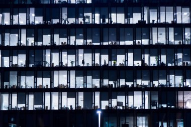 Geceleri ofis binası. Geç saatlere kadar işteydim. Cam perdeli ofis binası. Ofis binası gece geç saatlerde iç ışıklar açıkken. Ofis binasının ön cephesi