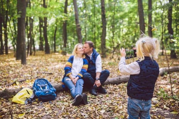 Utazás, turizmus, túrázás, technológia és családi koncepció. Boldog gyermek csinál fotó szülők az erdőben. Anya és apa pózolnak a fotón, a lány telefonon fotózik. Fiatal turistacsalád erdős területen — Stock Fotó