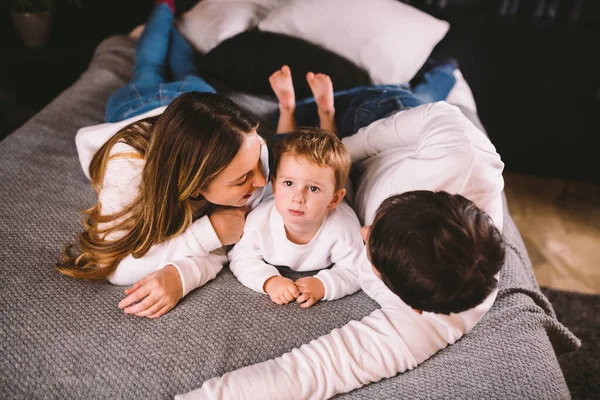 Glad familj har roligt i sovrummet. Njuter av att vara tillsammans. Föräldrarna kittlar sin son när de ligger i sängen. Glada familj leker tillsammans på sängen. Leende familj som har roligt — Stockfoto