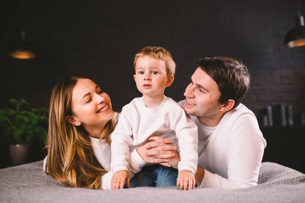 Positieve vrouwelijke en mannelijke hebben plezier samen met hun zoon in bed, genieten van kalme huiselijke sfeer en saamhorigheid. Familie brengt vrije tijd thuis door. Aantrekkelijke jonge familie in de slaapkamer — Stockfoto