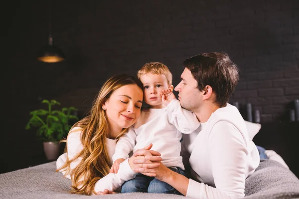 Gelukkig gezin heeft plezier in de slaapkamer. Genieten van het samenzijn. Ouders kietelen hun zoontje terwijl ze in bed liggen. Vrolijke familie die samen spelen op bed. Glimlachend gezin Veel plezier — Stockfoto