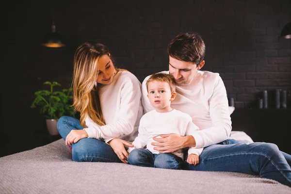 Positieve vrouwelijke en mannelijke hebben plezier samen met hun zoon in bed, genieten van kalme huiselijke sfeer en saamhorigheid. Familie brengt vrije tijd thuis door. Aantrekkelijke jonge familie in de slaapkamer — Stockfoto