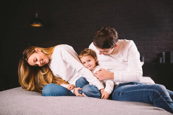 Föräldrar med sin lilla pojke i sängen hemma. Familjer med barn i sängen på natten hemma. Lycklig familj njuter i sängen. Mamma, pappa och barn leker i sovrummet på kvällen. Loft stil interiör — Stockfoto