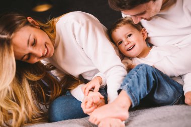 Mutlu aile yatak odasında eğleniyor. Birlikte olmanın tadını çıkarıyorum. Ebeveynler küçük oğullarını yatakta yatarken gıdıklıyorlar. Mutlu bir aile yatakta birlikte oynuyor. Gülümseyen Aile Eğleniyor