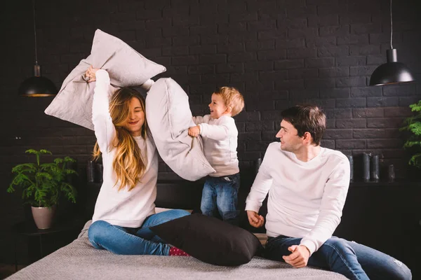 Family having funny pillow fight on bed. Parents spending free time with their son. Young family being playful at home. Happy parents and child. Young caucasian family fighting with pillows