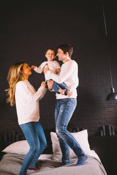 Family Jumping On Bed Together. Family fun. The beautiful family jumping on the bed. Caucasian mom dad and son active evening vacation at home, fun and joy at the weekend — 스톡 사진