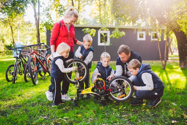 O tema é o trabalho em equipe e um espírito de família unido. Resolvendo problemas juntos. Grande família amigável reparar uma bicicleta no parque. Pai e mãe ensinam as crianças a usar ferramentas de ciclismo — Fotografia de Stock