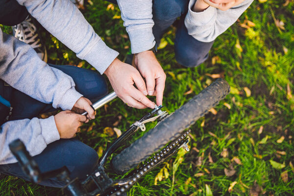 Father day. A large friendly family father and sons together actively relax in the fresh air. Dad teaches sons to repair bicycles. A child uses a tool on a sunny day in the courtyard