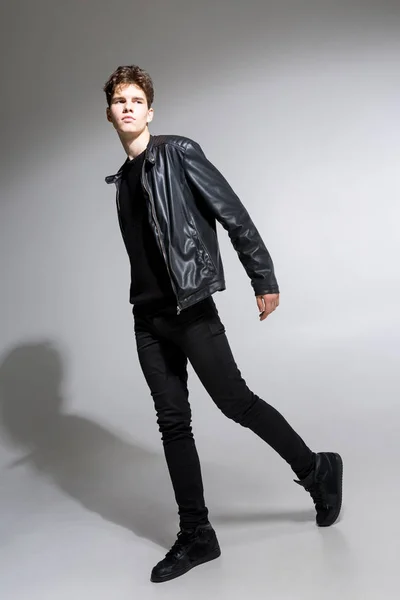 full length portrait of young fit man in dark cloths on the white background. Young Male Fashion Model Posing In Casual Outfit. Attractive young fashion model wearing black in leather jacket