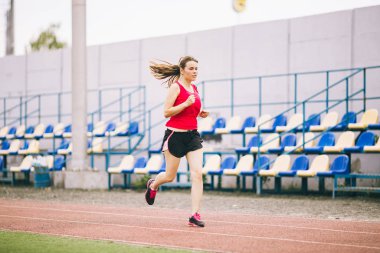 Stadyumda Koşan Kadın. Stadyum pistinde koşan genç bir kadın. Gol başarı konsepti. Spor sahasında spor koşusu. Sağlık teması. Kilo verme başarısı için spor antrenmanı kardiyosu
