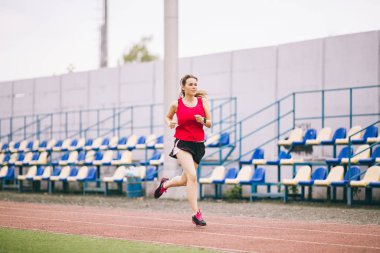 Stadyum pistinde koşan bayan koşucu, koşan ve dışarıda koşan kadın sporcu, spor ve fitness konsepti. Spor giyimli genç bir kadın stadyumda antrenman yapıyor. Spor yaşam tarzı konusu
