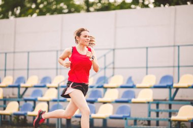 Stadyum pistinde koşan bayan koşucu, koşan ve dışarıda koşan kadın sporcu, spor ve fitness konsepti. Spor giyimli genç bir kadın stadyumda antrenman yapıyor. Spor yaşam tarzı konusu