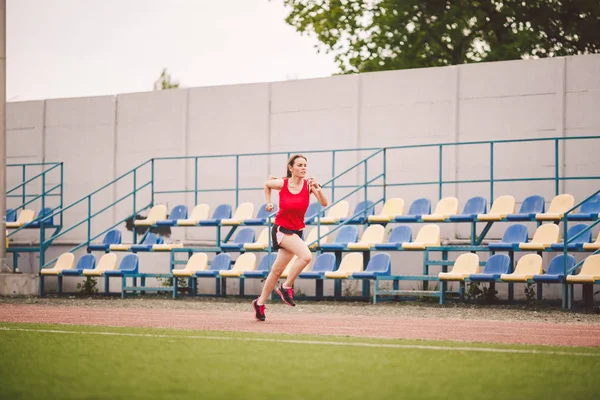 Corredor mujer corriendo en pista de estadio, atleta mujer corriendo y haciendo ejercicio al aire libre, deporte y concepto de fitness. Mujer joven en entrenamiento de ropa deportiva en un estadio. Tema de estilo de vida deportivo —  Fotos de Stock