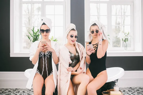 Thema Frauenfreundschaft. Party-Freundinnen, Entspannungs- und Wellness-Behandlungen, Junggesellenabschied. drei kaukasische schöne Frauen sitzen drinnen auf dem Badezimmer in Sonnenbrille, Kopftuch und Bademantel, Unterwäsche — Stockfoto