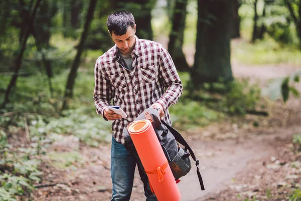 Tipo con mochila, viajero, hipster de pie en el bosque, Senderismo, Bosque, Viaje. Turista caucásico empaca mochila, toma cosas. Hombre descansando durante la caminata en madera. mirando en la bolsa de viaje — Foto de Stock